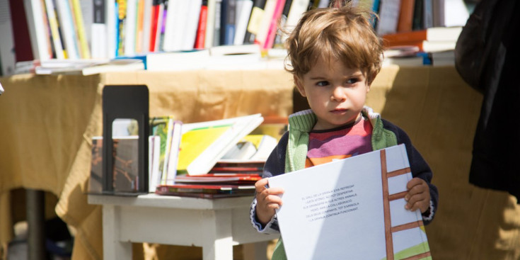 Un nen amb el llibre infantil ‘Alarma a la granja’ a les mans davant d’una parada de la plaça del Poble, ahir.