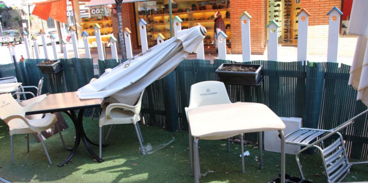 Para-sols i cadires de la terrassa d'un restaurant caiguts al terra, per l'efecte del vent.