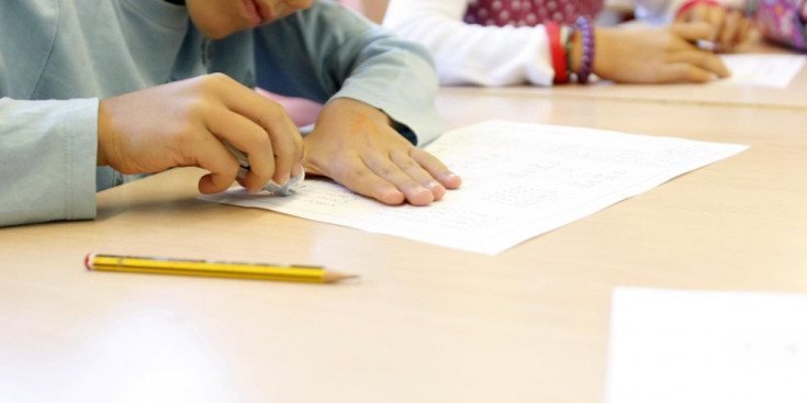 Un alumne treballa en una aula envoltat de companys.