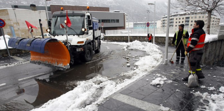 Operaris retiren la neu d’una vorera a la vegada que passa una llevaneu.