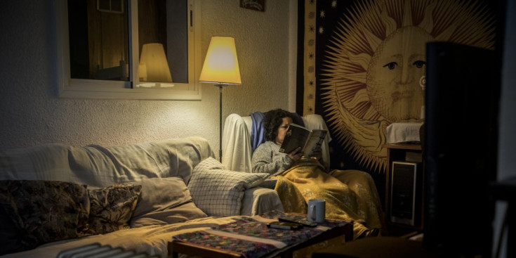 Una dona llegeix asseguda en una butaca de la sala d’estar del seu pis.