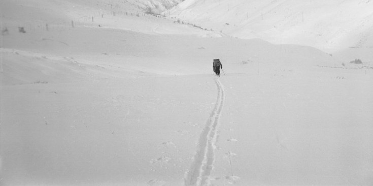 Un home carregat d’un farcell pesant avança esquiant cap al fons de la vall.
