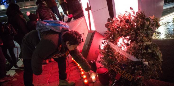 Un jove deixa una espelma davant la corona de flors pels drets socials.