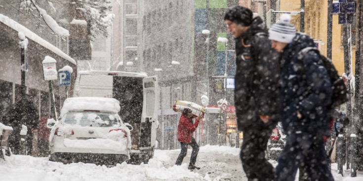 Una parella creua el carrer nevat enmig del temporal de neu i vent, ahir.