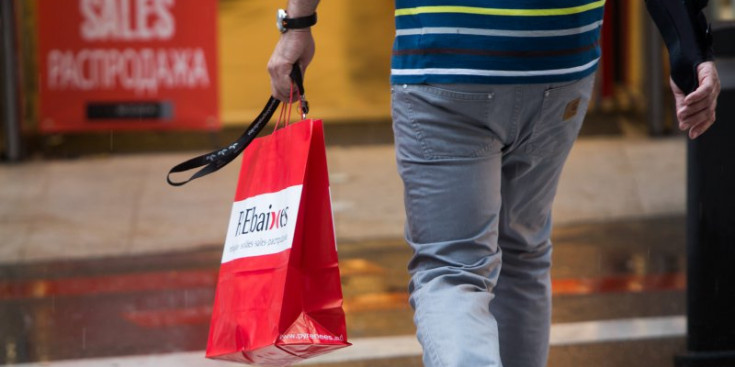 Un home creua un carrer de l’eix comercial amb una bossa després d’haver fet una compra.
