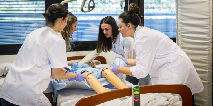 Quatre estudiants d’Infermeria fan pràctiques d’atenció als malalts amb un maniquí.