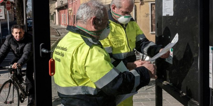 Funcionaris italians protegits amb mascaretes col·loquen uns cartells.