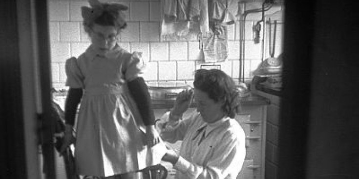 Una dona fent la vora d’una faldilla a una nena als anys 40.