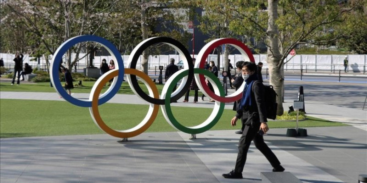 Un home passeja al costat de les anelles olímpiques que hi ha als afores de l’estadi olímpic de Tòquio.
