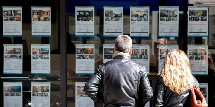 Una parella mira les ofertes de lloguer i venda d’habitatges a l’aparador d’una immobiliària.