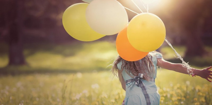 Imatge d’una nena que corre amb uns globus a les mans.