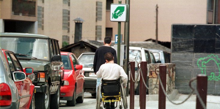 Ciutadà en cadira de rodes passant per una zona d’aparcament