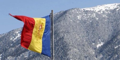 Imatge d’una bandera andorrana amb muntanyes nevades de fons.