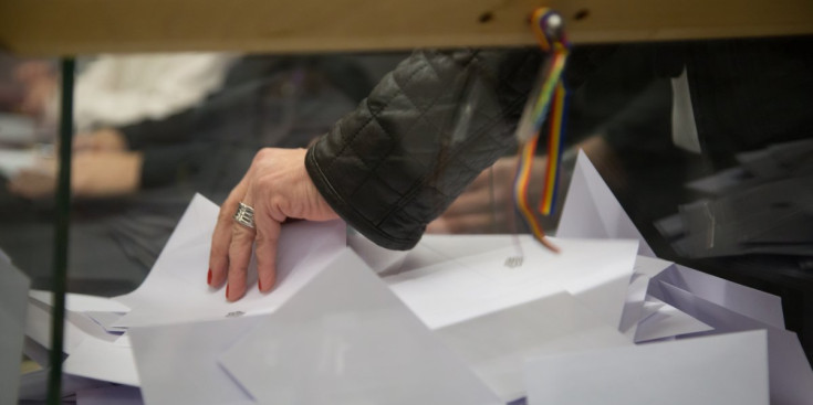Una dona agafa uns sobres de dins d’una urna electoral.