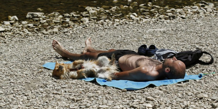 Un home i el seu gos prenen el sol a la riba d’un riu.