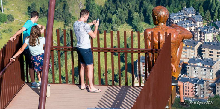 Un jove fa la foto a un altre que penja de l’estàtua del Roc del Quer.